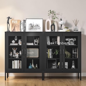 May include: Black metal cabinet with glass doors and mesh detailing. The cabinet is filled with books, decorative items, and a speaker. The top of the cabinet displays vases, a framed picture, and other decor. The text "OakTimberCo" is visible on the glass.