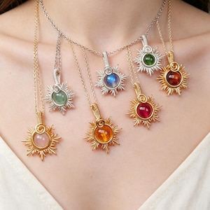 Puede incluir: Una colección de collares con colgantes de piedras preciosas. Cada collar presenta un diseño de sol con una piedra preciosa central y colorida. Los colgantes cuelgan de delicadas cadenas en tonos dorados y plateados. Las piedras incluyen rosa, naranja, rojo, verde y azul.