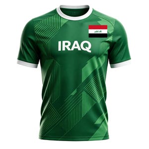 May include: Green athletic jersey with white trim and the word "IRAQ" in large white letters. The jersey features a geometric design and the Iraqi flag on the upper right chest. The shirt has short sleeves and a crew neck.