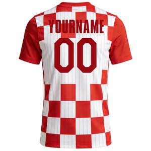 May include: A red and white chequered football shirt with red sleeves. The back displays the text "YOURNAME" above the number "00" in red. The shirt has a traditional athletic design.