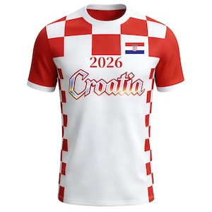 May include: White t-shirt with red chequered pattern on the shoulders and sides. The shirt features the text "2026 Croatia" in a colourful, outlined font, and the Croatian flag. The sleeves and collar are white.
