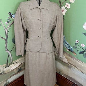 Könnte beinhalten: Ein beige-brauner karierter Rockanzug mit einer taillierten Jacke und einem knielangen Rock.