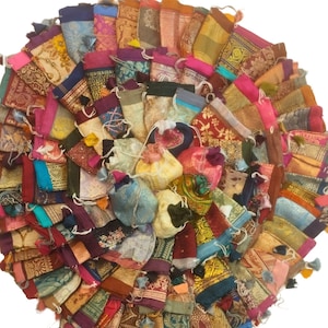 May include: A circular arrangement of small, colorful fabric pouches. The pouches are made from various patterned textiles in shades of red, pink, gold, blue, and green. Each pouch has a drawstring closure and some have small tassels.