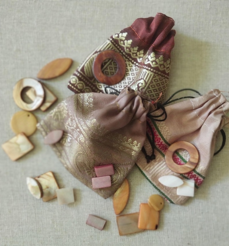May include: Two small fabric pouches with drawstring closures, filled with various wooden and shell-like shapes. The pouches are decorated with gold embroidery and have a brown and beige color scheme.