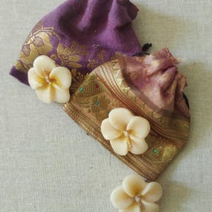 May include: Three white flower-shaped candles with a gold and purple fabric pouch in the background.