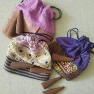 May include: Three small drawstring bags filled with brown incense cones. The bags are made of colorful patterned fabric. The bags are on a white surface.