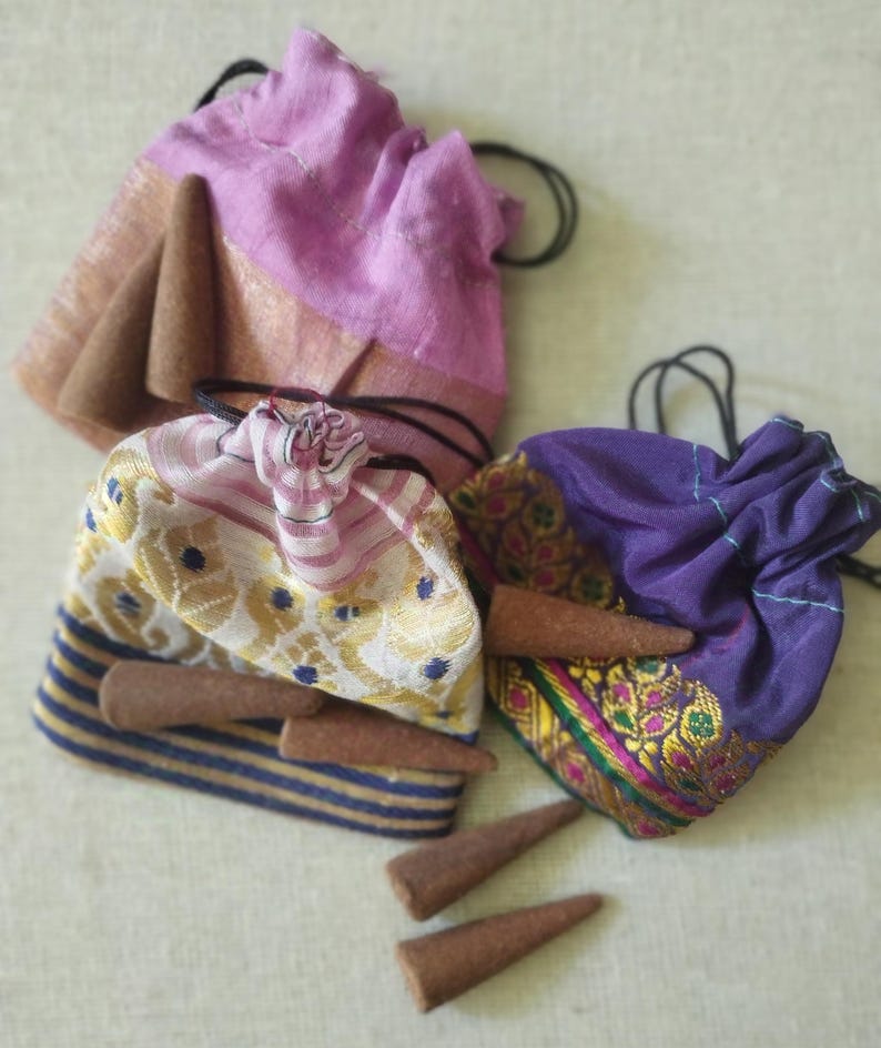 May include: Three small drawstring bags filled with brown incense cones. The bags are made of colorful patterned fabric. The bags are on a white surface.