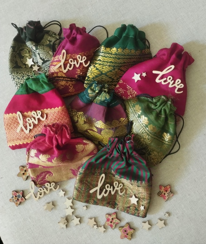 May include: A collection of eight small, colorful drawstring bags made of fabric with gold accents. Each bag has a wooden cutout of the word "love" attached to the front. The bags are surrounded by small wooden stars.