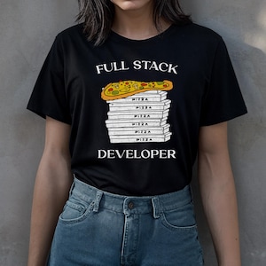 以下が含まれることがあります： 「FULL STACK DEVELOPER」の文字がプリントされた黒いTシャツ。ピザの箱が積み重ねられ、その上にピザが乗っているデザイン。ピザの箱には「PIZZA」の文字が書かれています。