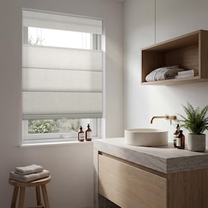 May include: A contemporary bathroom interior with a neutral colour scheme. A window with a Roman blind is visible. The wooden vanity unit has a stone countertop, a round sink, and a brass tap. Decorative bottles and a plant complete the look.