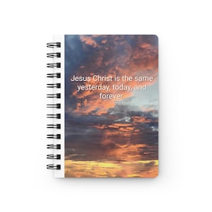 Puede incluir: Un cuaderno de espiral con una cubierta que presenta un cielo de puesta de sol. El texto "Jesucristo es el mismo ayer, hoy y siempre" está impreso en blanco. El cuaderno tiene una espiral blanca.