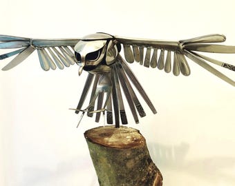 A bird of prey made with stainless steel cutlery, perched on a walnut branch. Unique piece.