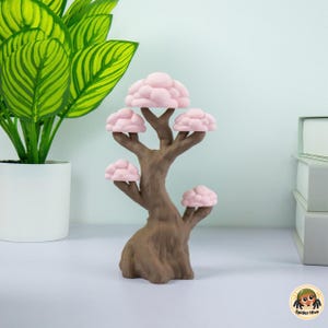 Peut inclure: Une sculpture d'arbre décorative dotée d'un tronc et de branches marron texturés, agrémentés de cinq grappes de feuillage arrondies et rose clair en forme de nuages. L'objet se tient droit sur une base large, représentant une forme d'arbre stylisée.