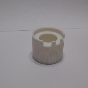 May include: A white, cylindrical object with a textured, basket-weave pattern on the exterior. The top has a circular opening and a crenelated edge, resembling a miniature castle. The object is likely a decorative or functional item.
