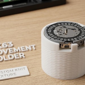 May include: A white VK63 movement holder with a custom knit texture, holding a watch movement. The watch movement has a silver face with black and white markings. The text "VK63 MOVEMENT HOLDER" and "CUSTOM KNIT TEXTURE" are also visible.