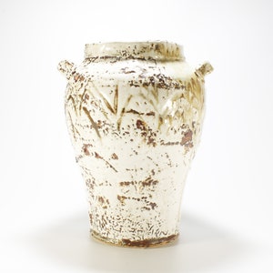 May include: A white ceramic vase with brown accents and a textured surface. The vase has two handles and a rounded body.