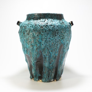 May include: A teal and black ceramic vase with a textured surface and two small handles. The vase has a unique, dripping glaze effect.