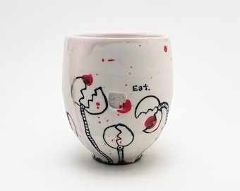 Puede incluir: Taza de cerámica blanca con salpicaduras rojas y negras e ilustraciones dibujadas a mano de huevos con el texto "Eat."