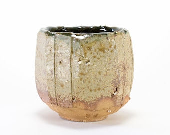 Puede incluir: Una taza de cerámica rústica, hecha a mano, con un esmalte marrón claro y un borde marrón oscuro. La taza tiene una superficie texturizada y una forma ligeramente irregular.