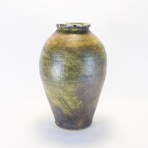 May include: A handcrafted ceramic vase with a textured surface. The vase features a gradient of colors, transitioning from a dark brown base to olive green and tan near the top. The opening has a slightly rough, off-white rim.