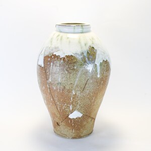 May include: A handcrafted ceramic vase with a unique design. The vase features a light brown base with white and green accents, and a white rim. The design includes geometric shapes and a textured surface, adding to its artistic appeal.