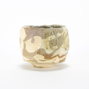 May include: A small, ceramic bowl with a rough, textured surface. The bowl is decorated with a swirling pattern of brown, white, and beige glaze.