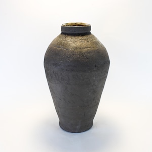 May include: A dark gray ceramic vase with a textured surface. The vase has a rounded body that tapers towards the base and a cylindrical neck. The rim of the vase has a gold-colored interior.