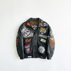 以下が含まれることがあります： 黒い革のジャケット。タイガー、ワシ、ブルドッグなどのパッチが複数付いています。ジャケットは襟付きで、ボタン留めです。「Wicked」と「Grease」の文字が入ったパッチがあります。