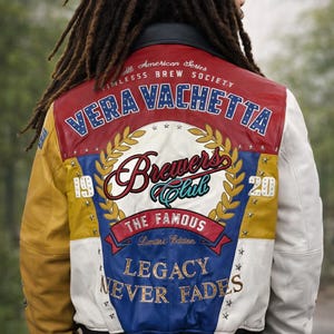 May include: A multi-colored leather jacket with a design on the back. The jacket features red, white, yellow, and blue panels. Text on the back includes "VERA VACHETTA", "Brewers Club", and "LEGACY NEVER FADES".
