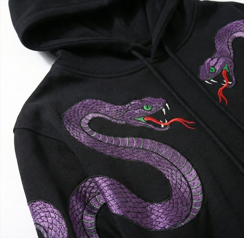 May include: Black hooded sweatshirt with embroidered purple snakes. The snakes have green eyes and red tongues, creating a striking contrast. The design is repeated on the front and sleeve. The hood is visible.