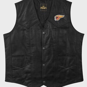 May include: A black leather waistcoat featuring a V-neckline, four front snap button closures, and two lower pockets. A small, colourful embroidered patch of a winged head is positioned on the upper left chest. The interior label reads AMERICA.