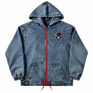 May include: A blue acid-wash denim zip-up hoodie featuring a bright red front zip and matching red drawstring at the hem. The garment includes a black and white graphic patch of a horned creature on the chest and a small black logo tag at the hem.