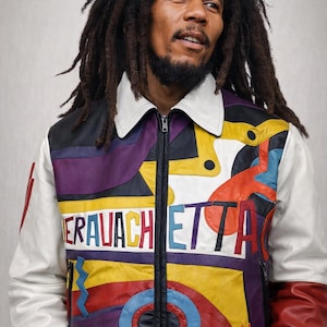 Puede incluir: Una chaqueta de cuero colorida con la palabra "ERAVACHETTA" en el pecho. La chaqueta tiene cuello y mangas blancos, con cremallera y ribete negros. El diseño incorpora formas geométricas moradas, amarillas, rojas y azules.