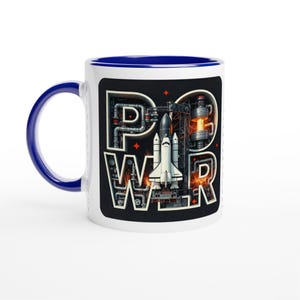 Pode incluir: Caneca de cerâmica branca com interior e alça azuis. A caneca apresenta a palavra "POWER" em um design mecânico e industrial com uma ilustração de um ônibus espacial em um fundo preto.