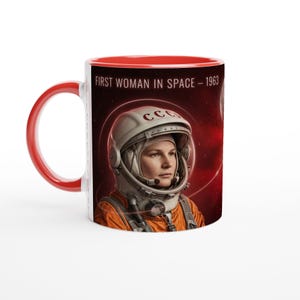 Könnte beinhalten: Eine Keramiktasse mit leuchtend rotem Henkel und rotem Innenraum. Die Außenseite zeigt eine Grafik eines Astronauten mit weißem Helm und der Aufschrift CCCP, in einem orangefarbenen Anzug vor rotem Weltraumhintergrund. Der Text lautet FIRST WOMAN IN SPACE – 1963.