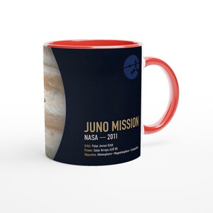 Könnte beinhalten: Ein Keramikbecher mit leuchtend rotem Innenraum und Henkel, verziert mit einer dunkelblauen Grafik des Planeten Jupiter und dem Text Juno Mission NASA 2011. Das Design enthält Missionsdetails wie Orbit: Polar Jovian Orbit und Power: Solar Arrays (420 W).