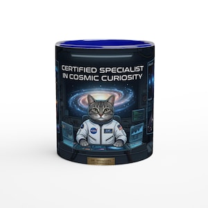 Op de afbeelding: Een keramische mok met een blauw interieur en een rondom ontwerp. Het ontwerp toont een grijze tabby kat in een NASA-ruimtepak, met de tekst "CERTIFIED SPECIALIST IN COSMIC CURIOSITY". De mok heeft een melkwegachtergrond.