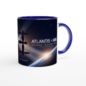 Könnte beinhalten: Ein dunkelblauer Keramikbecher mit einer Weltraumgrafik der Raumstation Mir vor einem Sternenhintergrund und dem Horizont der Erde. Der Text lautet ATLANTIS x MIR, First Docking - 29 June 1995 - STS-71, A New Era of International Cooperation.
