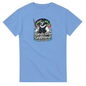 Puede incluir: Camiseta azul claro con un gráfico de un oso polar con un chaleco táctico y una lanza. El oso está sobre un fondo de la Aurora Boreal, con el texto "Hands Off Greenland" y "GDF Activated".