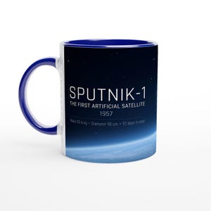 Pode incluir: Uma caneca de cerâmica branca com interior e alça azuis. A caneca apresenta o texto "SPUTNIK-1" e "THE FIRST ARTIFICIAL SATELLITE 1957" sobre um fundo azul escuro com uma representação da Terra. O diâmetro da caneca é de 58 cm.