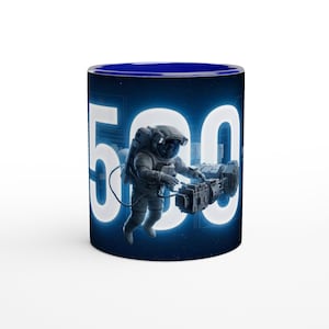 Op de afbeelding: Een cilindrische keramische mok met een diepblauwe binnenkant en een donkerblauw buitenoppervlak met een ruimte-thema. Het ontwerp toont het grote witte getal 500 met een astronaut die ervoor zweeft en een mechanisch apparaat vasthoudt.