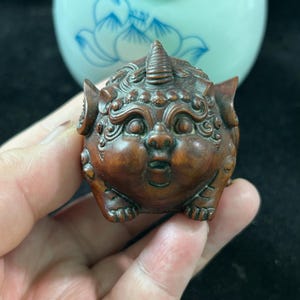 Può includere: Statuetta in legno intagliata a mano raffigurante una creatura mitica con un corno, grandi orecchie e un'espressione sorpresa. La statuetta è di colore marrone scuro e presenta dettagli intricati.