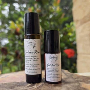 May include: Two small, dark brown glass roll-on bottles with black caps. The bottles have white labels with the text "Golden Rise" and ingredient information. The larger bottle contains 10 ml, and the smaller bottle contains 5 ml.