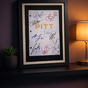 May include: Framed script from "The Pitt" episode, featuring multiple signatures in black, blue, and red ink. The title "THE PITT" is in gold lettering. The frame is black with a cream-colored mat.