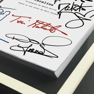 May include: A close-up of a book titled "Coraline" with multiple signatures in black, blue, and red ink. The book's title is in a stylized font, and the cover features the names of the screenplay writer and the author of the novel.