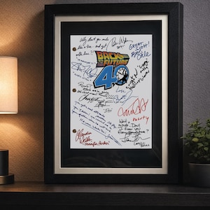 May include: Framed artwork featuring the "Back to the Future" logo with the number "40" and numerous signatures. The artwork is in a black frame with a white mat, displayed on a dark surface.