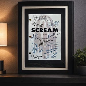 Pode incluir: Roteiro do filme "Scream" emoldurado com assinaturas. A moldura preta envolve um roteiro branco com o título "Scream" em letras em negrito. O roteiro é assinado por várias pessoas. Uma lâmpada e uma planta estão no fundo.