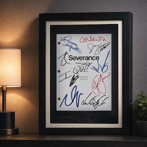 May include: Framed print of a "Severance" script page, featuring multiple signatures in blue and red ink. The black frame has a white matting, and the print is displayed on a dark surface with a lamp and plant in the background.