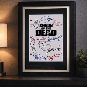 Può includere: Stampa incorniciata del film "Shaun of the Dead" con più firme in vari colori. Il titolo è in grassetto nero e le firme sono in inchiostro blu, rosso e nero. La cornice è nera con un bordo interno dorato.