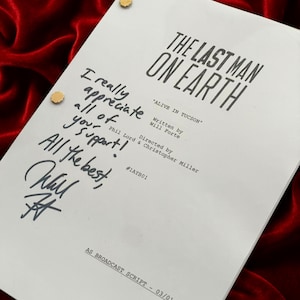Può includere: Una sceneggiatura bianca per "The Last Man on Earth" con il titolo in grassetto nero. La sceneggiatura include note manoscritte e una firma. La sceneggiatura è tenuta ferma con elementi di fissaggio color oro, su uno sfondo di velluto rosso.